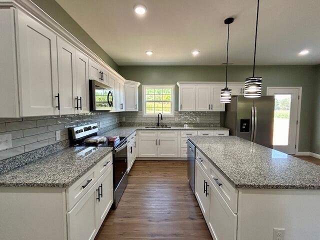 kitchen featuring pendant lighting, a center island, white cabinets, light stone countertops, and appliances with stainless steel finishes