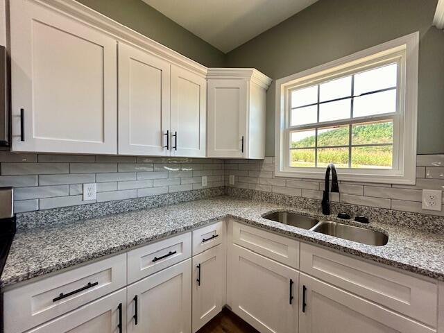 kitchen featuring decorative backsplash, white cabinetry, sink, and light stone countertops