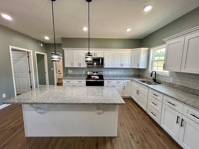 kitchen with decorative light fixtures, stainless steel appliances, a kitchen island, and sink