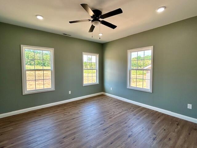 spare room with a healthy amount of sunlight, ceiling fan, and dark wood-type flooring