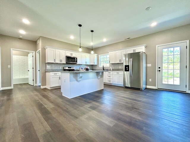 kitchen with a center island, white cabinets, hanging light fixtures, appliances with stainless steel finishes, and a kitchen bar