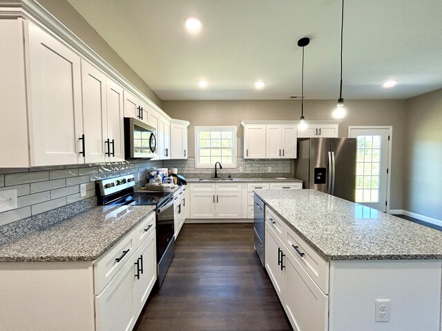 kitchen with white cabinetry, sink, a center island, stainless steel appliances, and decorative light fixtures