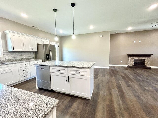 kitchen with light stone countertops, stainless steel appliances, white cabinetry, hanging light fixtures, and a stone fireplace