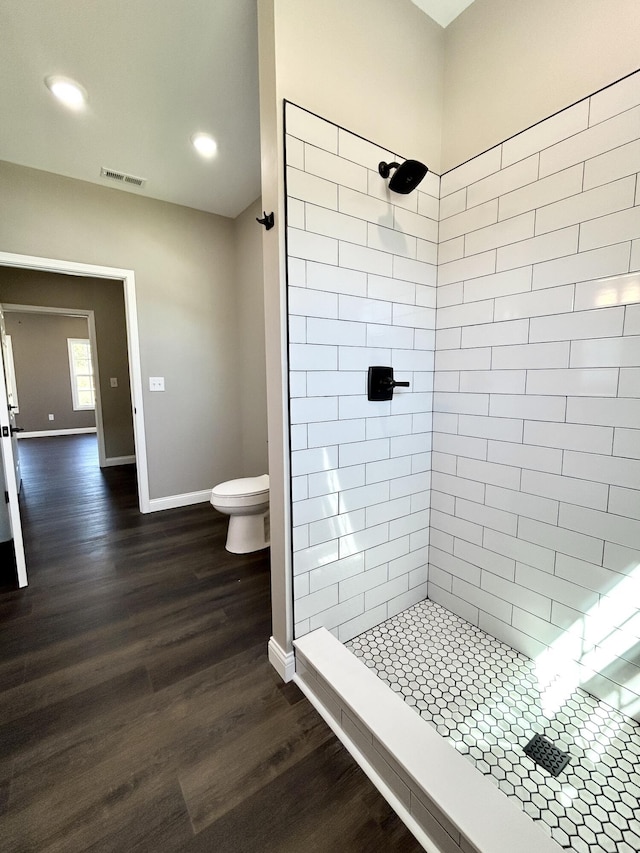 bathroom with a tile shower, toilet, and wood-type flooring