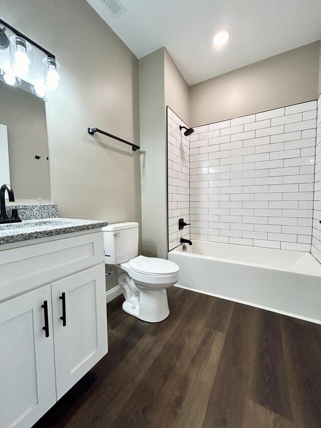 full bathroom with tiled shower / bath, hardwood / wood-style flooring, vanity, and toilet