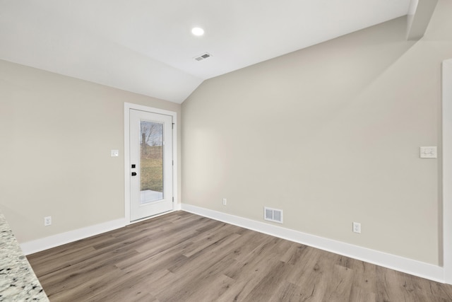 spare room with lofted ceiling, light wood finished floors, visible vents, and baseboards