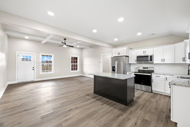 kitchen with sink, a kitchen island, white cabinets, stainless steel appliances, and backsplash