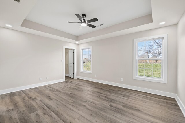 unfurnished room with a raised ceiling, wood-type flooring, and ceiling fan