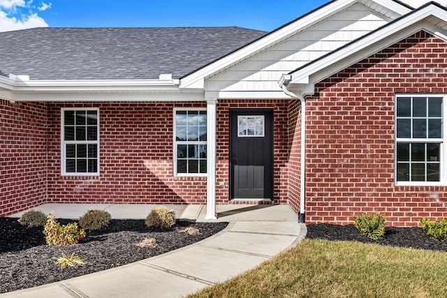 view of exterior entry featuring brick siding and roof with shingles