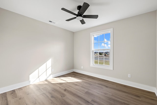 empty room with a ceiling fan, wood finished floors, visible vents, and baseboards