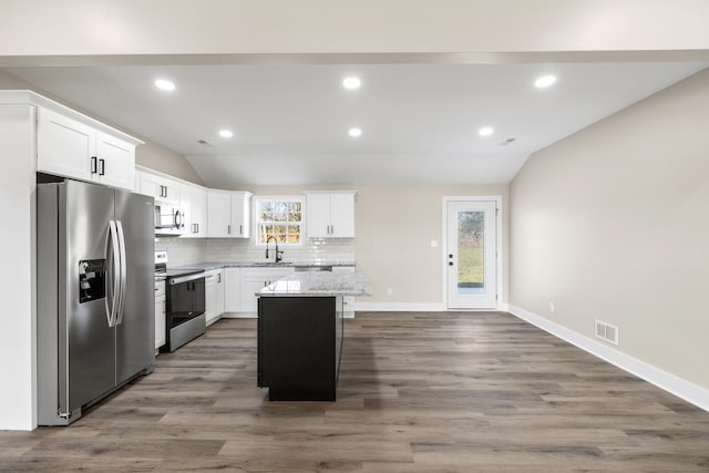 kitchen featuring white cabinetry, lofted ceiling, a center island, stainless steel appliances, and light stone countertops