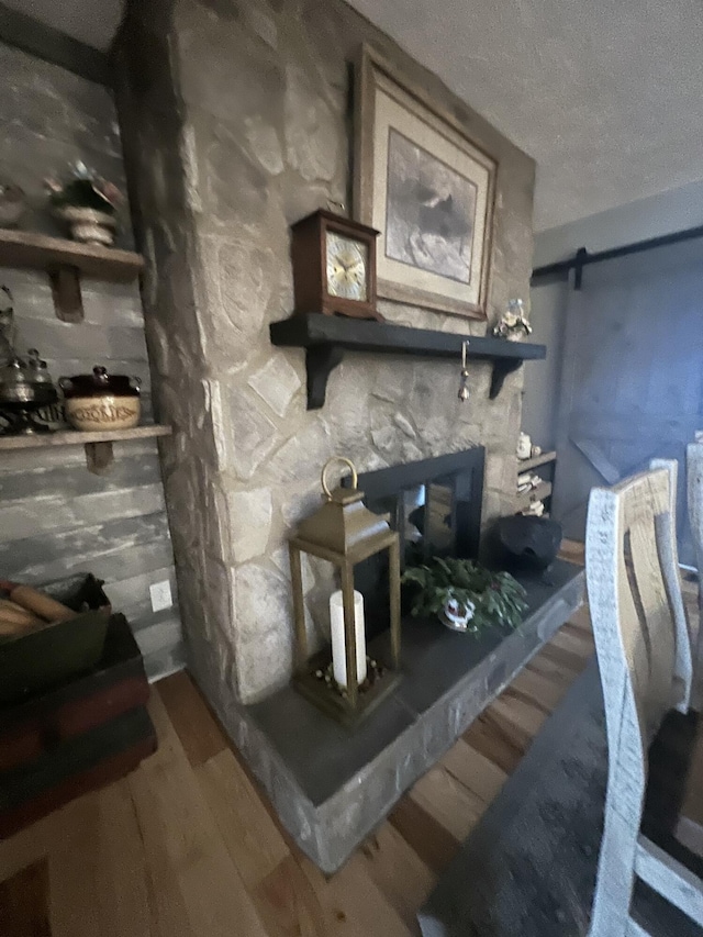 misc room featuring a barn door, a stone fireplace, hardwood / wood-style floors, and a textured ceiling