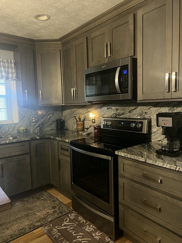 kitchen with a textured ceiling, dark hardwood / wood-style floors, stainless steel appliances, and dark stone counters