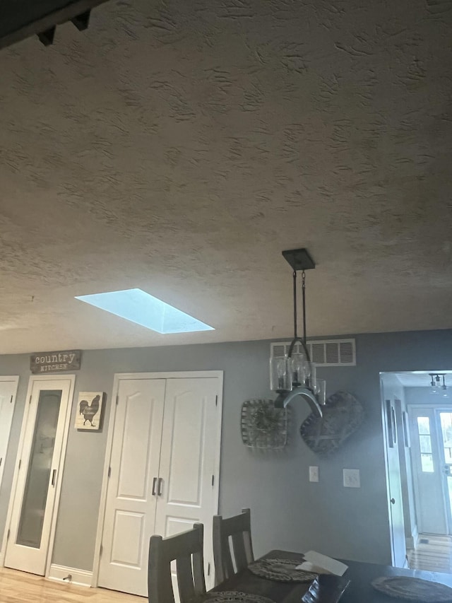 unfurnished dining area featuring wood-type flooring, a textured ceiling, and a skylight