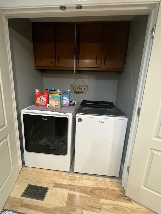 clothes washing area featuring cabinets, washing machine and dryer, and light hardwood / wood-style flooring