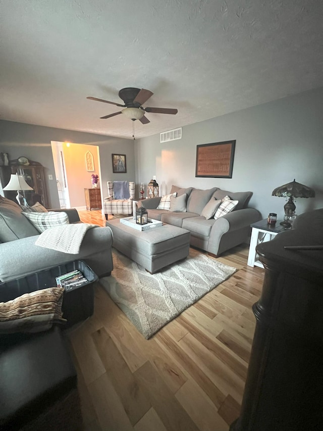 living room with a textured ceiling, light hardwood / wood-style floors, and ceiling fan