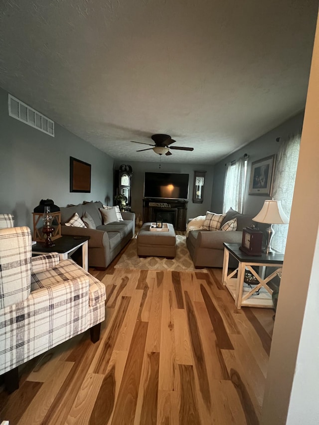 living room with hardwood / wood-style floors, ceiling fan, and a textured ceiling