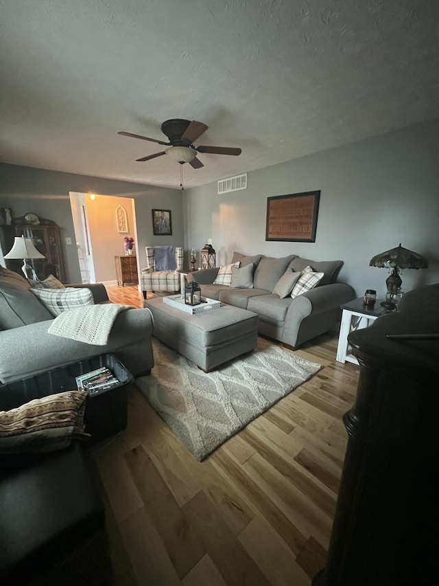 living room featuring ceiling fan, a textured ceiling, and light wood-type flooring