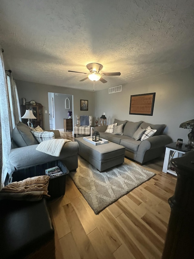 living room with ceiling fan, a textured ceiling, and hardwood / wood-style flooring