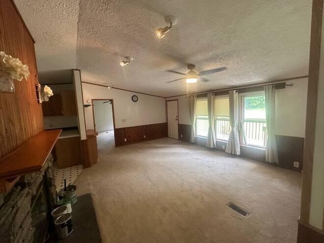 unfurnished living room with carpet, wooden walls, ceiling fan, and a textured ceiling