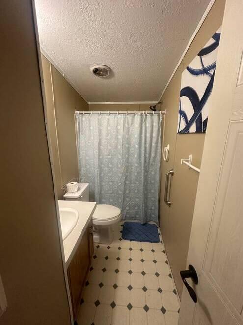 bathroom with vanity, curtained shower, toilet, and a textured ceiling