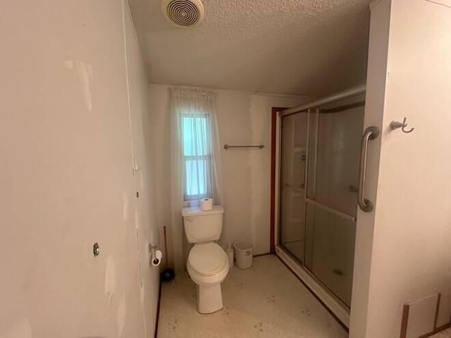 bathroom with a shower with door, a textured ceiling, and toilet