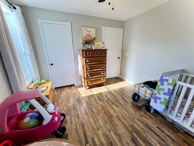 bedroom featuring hardwood / wood-style floors, ceiling fan, a crib, and a textured ceiling