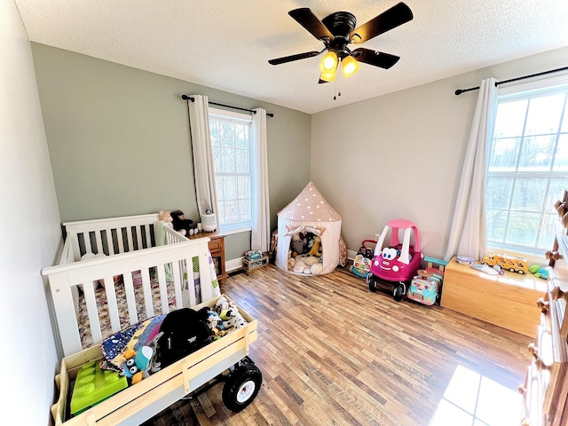 bedroom featuring ceiling fan, a nursery area, a textured ceiling, and wood-type flooring