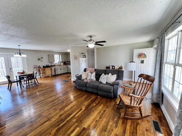 living room with french doors, ceiling fan with notable chandelier, a wealth of natural light, and dark wood-type flooring