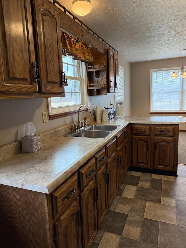 kitchen featuring a textured ceiling, kitchen peninsula, sink, and decorative light fixtures