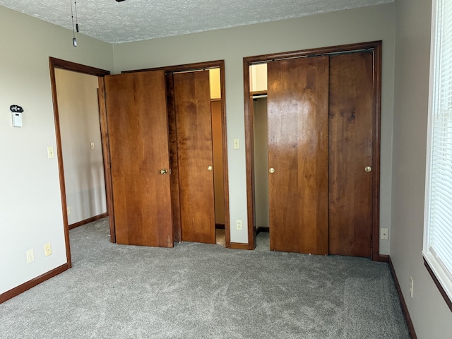 unfurnished bedroom with light carpet, a textured ceiling, and multiple closets