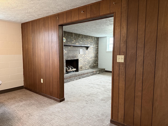 unfurnished living room with a textured ceiling, light colored carpet, a fireplace, and wooden walls