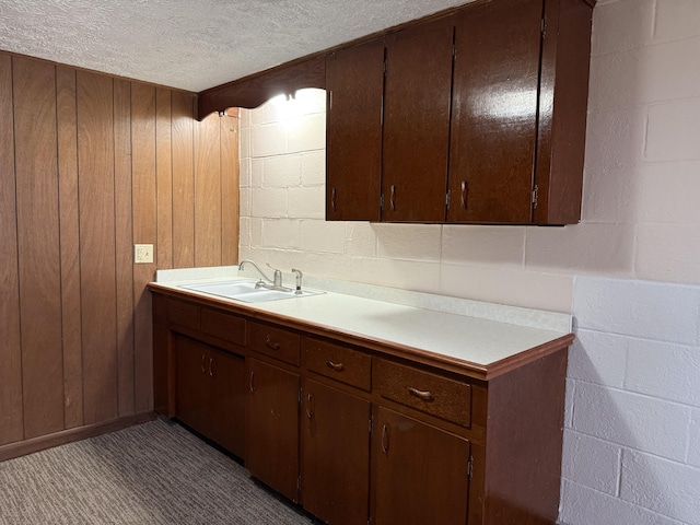 kitchen with a textured ceiling, wood walls, dark brown cabinetry, and sink