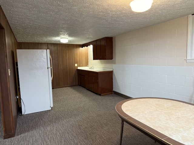 kitchen featuring a textured ceiling, sink, white refrigerator, tile counters, and wood walls