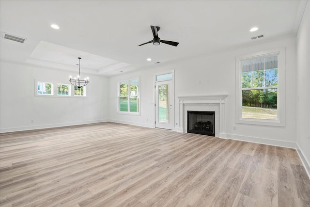 unfurnished living room featuring a raised ceiling, plenty of natural light, light hardwood / wood-style floors, and ceiling fan with notable chandelier