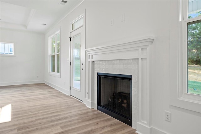 unfurnished living room featuring a raised ceiling, a tiled fireplace, and light hardwood / wood-style floors