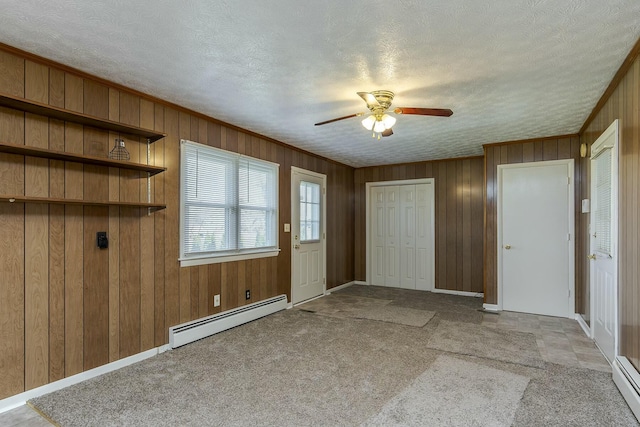 carpeted foyer featuring ceiling fan, baseboard heating, wood walls, and a textured ceiling