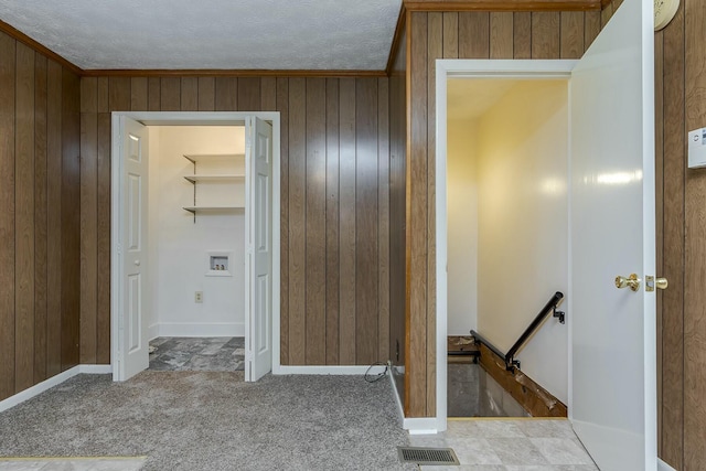 hallway featuring light carpet, a textured ceiling, and wooden walls