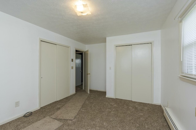 unfurnished bedroom with a baseboard heating unit, multiple closets, and carpet flooring