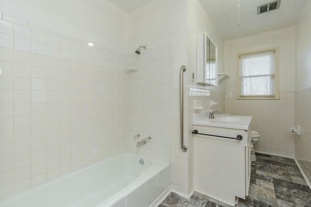 full bathroom with tile walls, toilet, vanity, and tiled shower / bath