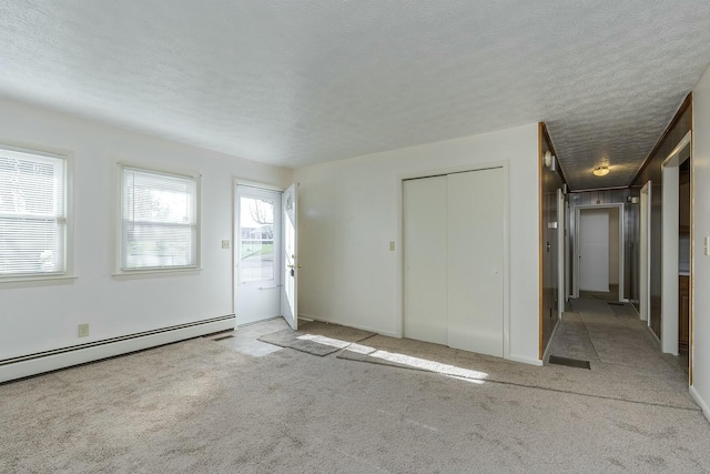 carpeted empty room featuring a textured ceiling and a baseboard heating unit