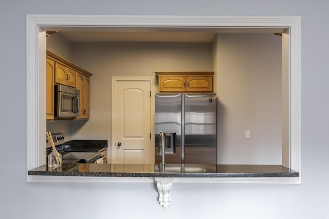 kitchen featuring stainless steel appliances, a peninsula, brown cabinetry, and dark stone countertops