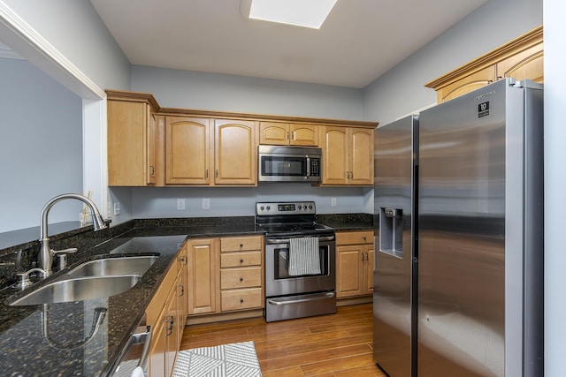 kitchen with a sink, appliances with stainless steel finishes, dark stone countertops, and dark wood finished floors