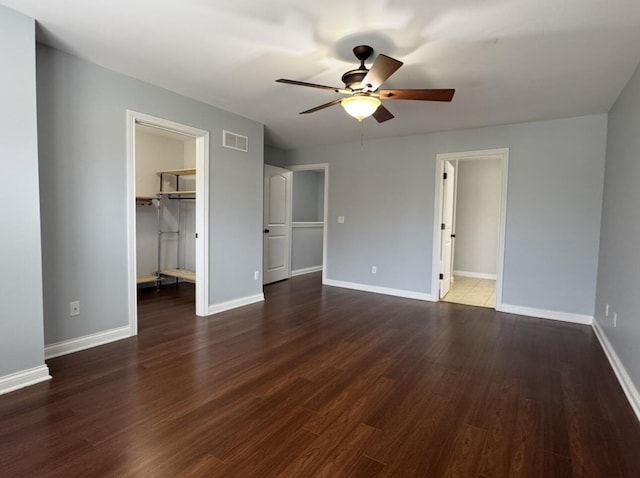 unfurnished bedroom featuring a spacious closet, visible vents, baseboards, and wood finished floors