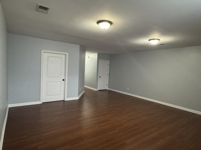 empty room with dark wood-type flooring, visible vents, and baseboards