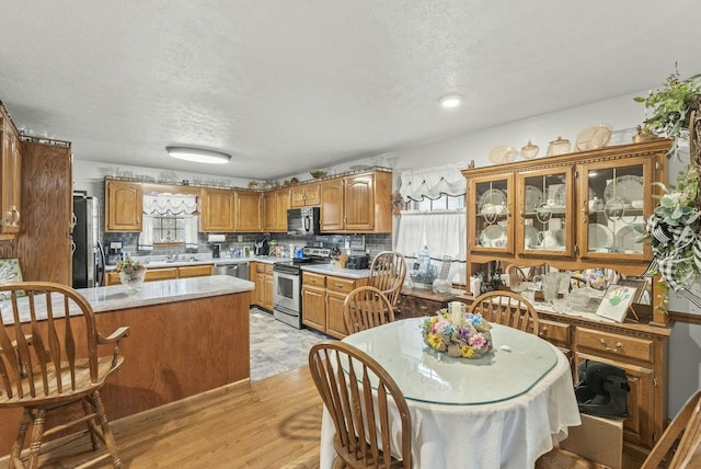 kitchen featuring sink, stainless steel appliances, backsplash, light hardwood / wood-style floors, and a textured ceiling