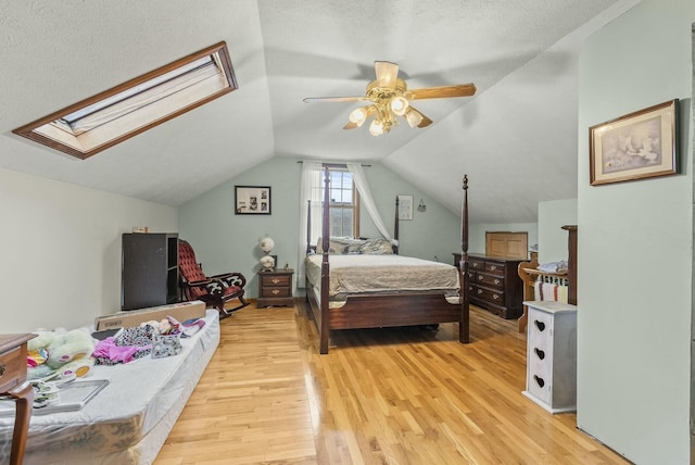 bedroom with vaulted ceiling with skylight, ceiling fan, a textured ceiling, and light hardwood / wood-style flooring