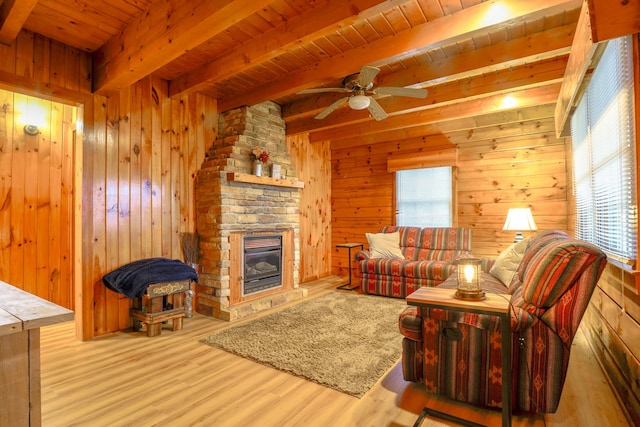 living room featuring ceiling fan, wooden ceiling, beamed ceiling, wooden walls, and a fireplace