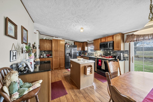 kitchen with appliances with stainless steel finishes, light wood-type flooring, ornamental molding, decorative light fixtures, and a center island