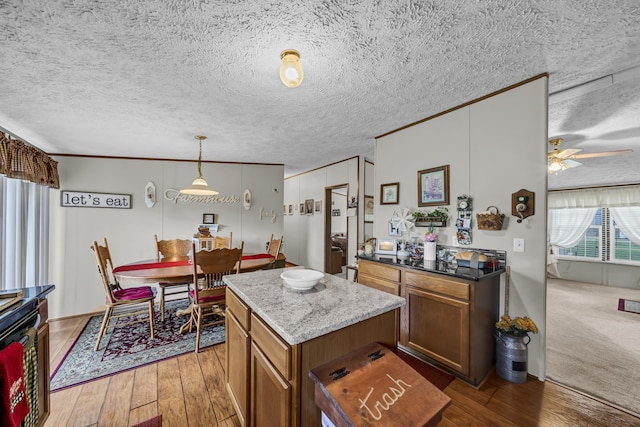 kitchen featuring light stone countertops, ceiling fan, wood-type flooring, decorative light fixtures, and a center island